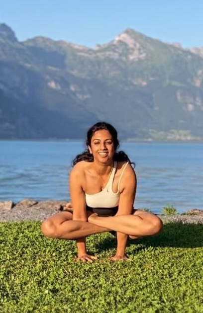 Gana in einer tiefen Hocke im Gras am Walensee, dahinter die Berge.